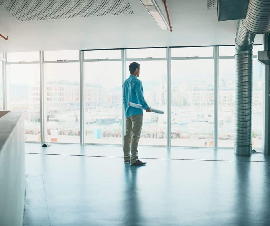 Owner stands in empty office with blueprints for ways to boost revenue for vacant office space.