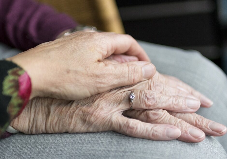 MN budget and senior care implications is depicted by young hand resting on senior's hand