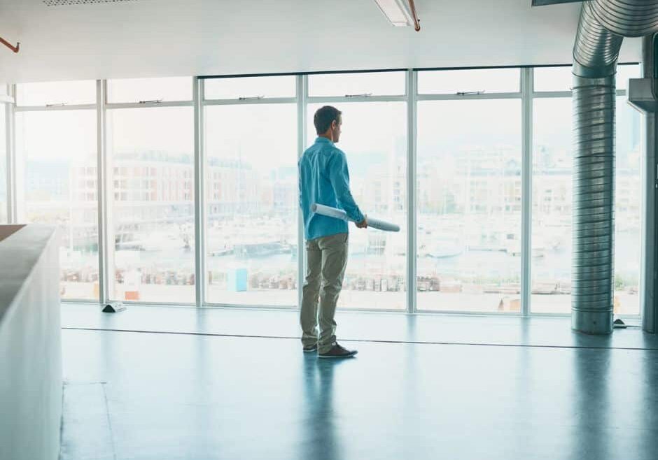 Owner stands in empty office with blueprints for ways to boost revenue for vacant office space.