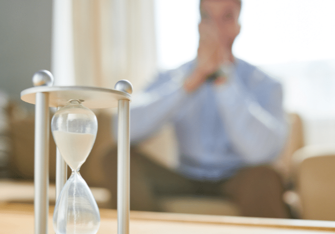 Waiting for commercial construction costs to decrease, stressed out business man watches time pass through hourglass.